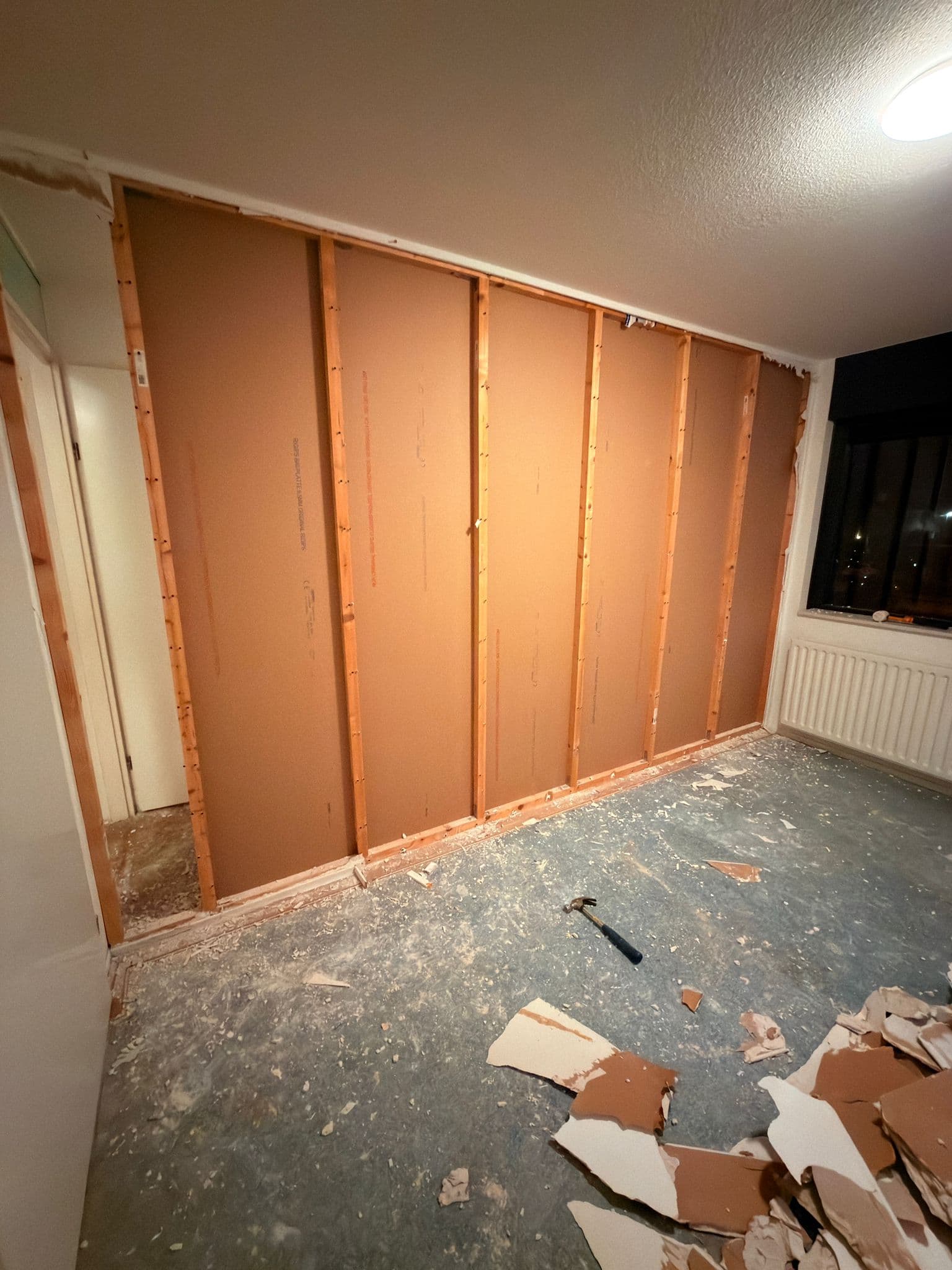 Interior room renovation with exposed wooden wall studs and drywall debris scattered on the floor.