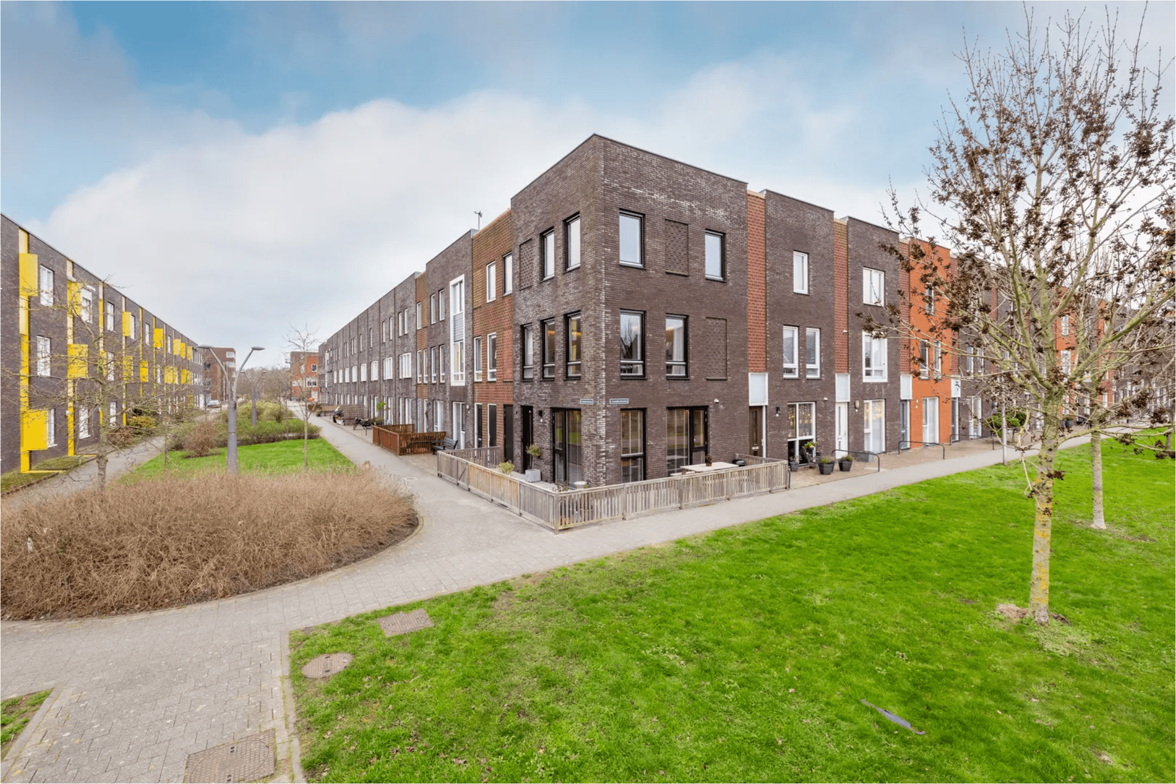 Modern multi-story brick townhouses with large windows face a green lawn and paved walkways.