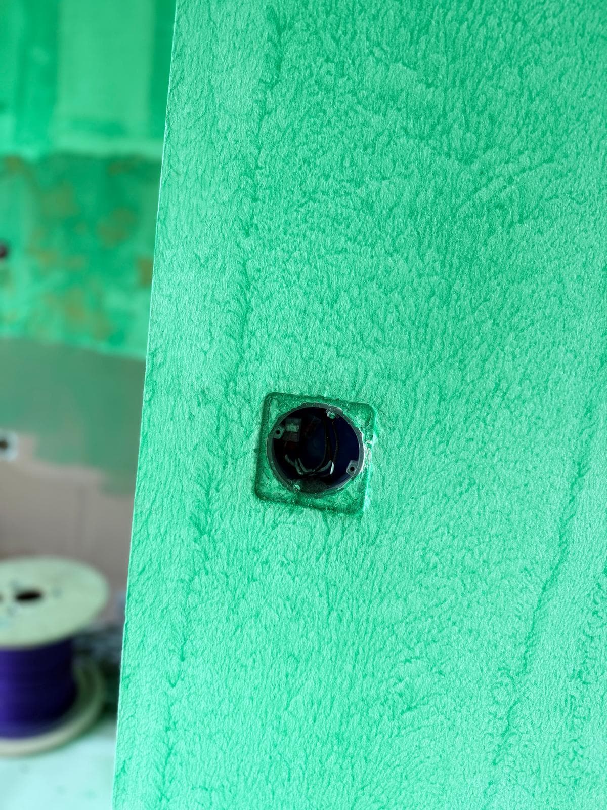 Bright green textured wall with a recessed circular electrical junction box and exposed wiring.