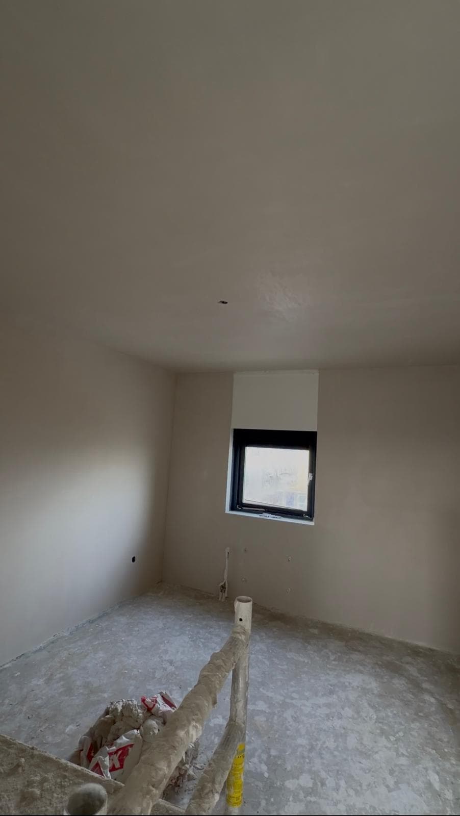 Unfinished room with plastered walls, a small window, and a dusty concrete floor.