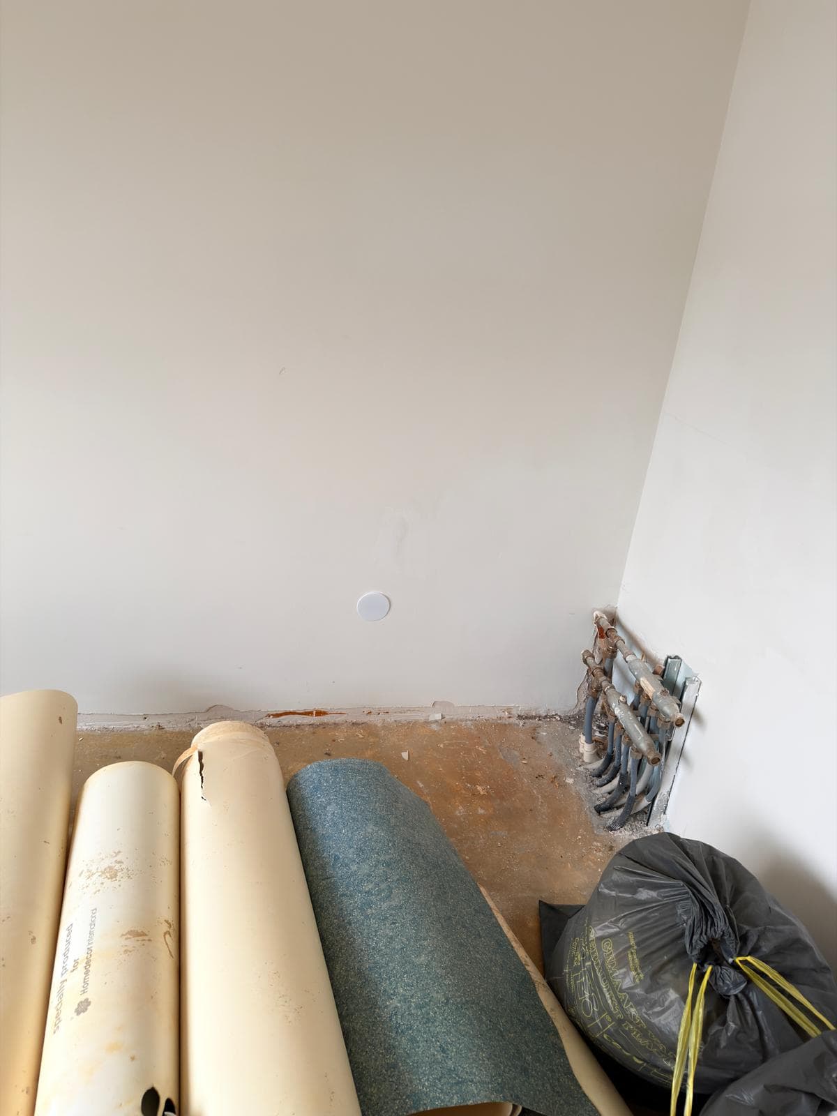 Rolls of flooring and exposed plumbing pipes in a white room undergoing renovation.